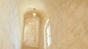 Un escalier en pierre menant vers le haut, dans un bâtiment doté de fenêtres en arc de cercle et d’un luminaire au sommet.