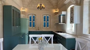 Une cuisine avec des meubles de couleur turquoise, une table à manger blanche et un lustre.