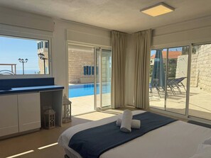 Une chambre d’hôtel comprenant un lit, un bureau, une vue sur une piscine et un balcon aménagé avec du mobilier d’extérieur.