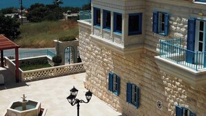 Un bâtiment en pierre de deux étages, avec un toit recouvert de tuiles rouges, des volets bleus et un balcon.