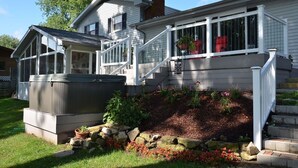 A two-story house with a covered porch, a small garden with flowers and rocks, and a hot tub in the front yard.