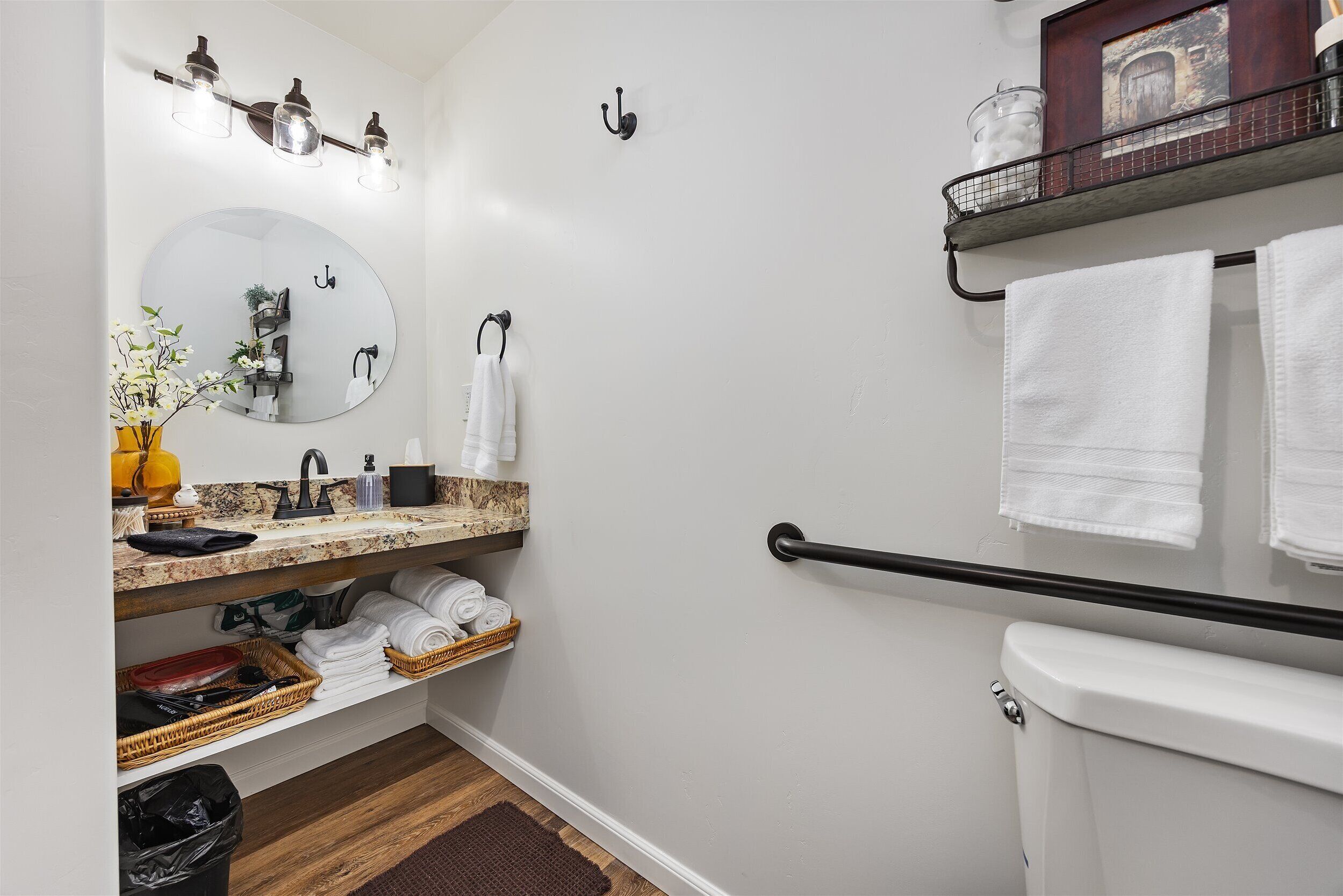 Ein modernes Badezimmer mit rundem Spiegel, Waschbecken mit Marmorplatte, Toilette und Handtuchhalter.