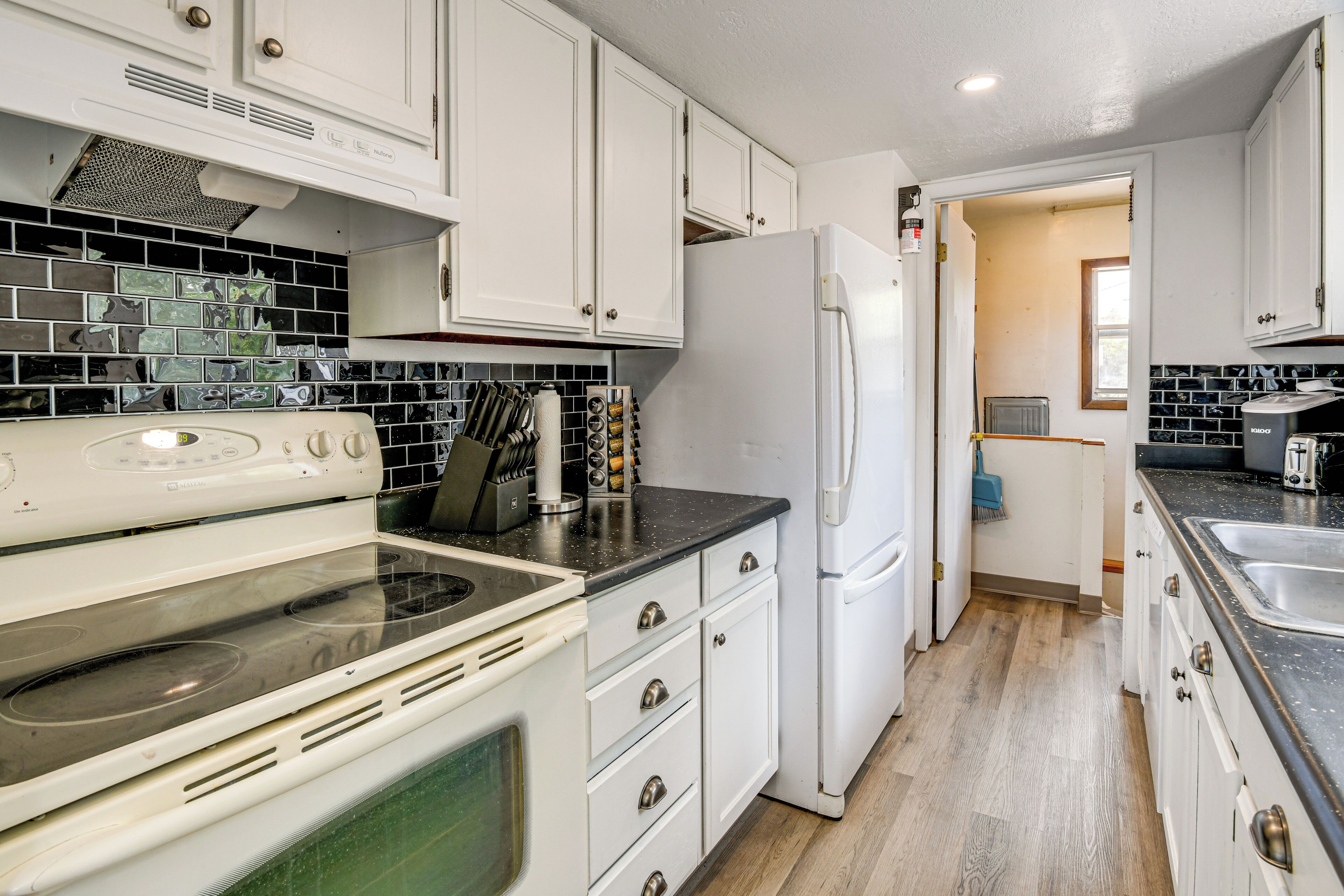 A kitchen with white cabinets, a black countertop, and a tiled backsplash.