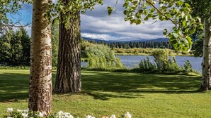 A serene outdoor setting with birch trees, a grassy area, and a lake with mountains in the background. - Black Butte Ranch `Trip House` On the Golf Course (Sisters)