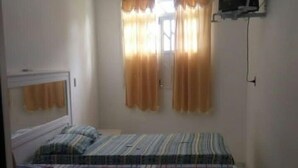 Un dormitori amb un llit, una finestra amb cortines i una televisió penjada a la paret.