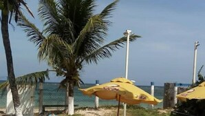 Un pati al costat de la platja amb un parasol groc, cadires de plàstic blanc i vista a l'oceà.