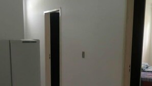Un passadís amb terres i parets de rajoles blanques, que condueix a una habitació amb un llit i una finestra.