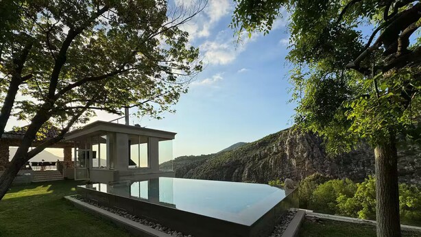 Una casa moderna con una piscina infinita de vidrio, rodeada por un césped cuidado y árboles.