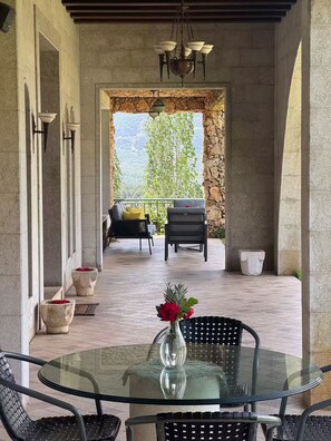 A covered outdoor seating area with a glass table, chairs, and a vase with flowers. - Casa Del Sultan Infinity Pool Garden Private (North Governorate)