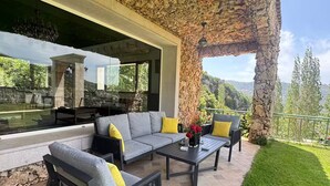 Un área de estar al aire libre con un fondo de pared de piedra, un banco de piedra y vistas a un paisaje montañoso.