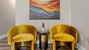 A hallway with two gold velvet chairs, a small table with a potted plant, and a colorful abstract painting on the wall.