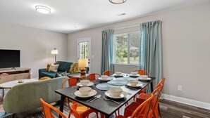 A dining area with a table set for four, surrounded by orange chairs, and a television in the background.