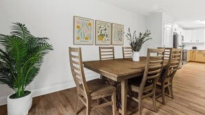 Un comedor con una mesa y sillas de madera, una planta en maceta y tres cuadros colgados en la pared.