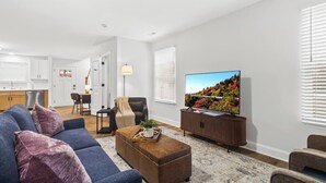 Una sala de estar moderna con un sofá, un reposapiés y un televisor de pantalla plana sobre un mueble de madera.