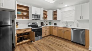 Una cocina moderna con armarios blancos, un refrigerador de acero inoxidable, horno empotrado, microondas y lavavajillas.