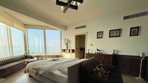 Une chambre spacieuse avec un grand lit, un canapé sombre et une vue sur la ville grâce à de grandes fenêtres.