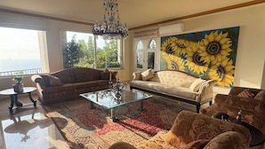 Un salon spacieux avec un grand canapé, une table basse et un lustre. Un grand tableau représentant des tournesols est accroché au mur.