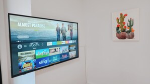 A television mounted on a wall displaying a streaming service interface with various content options. - 2 King Beds / 55" TV / Rainfall Shower / W/D (Philadelphia)