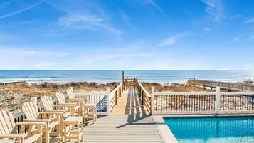Una terraza de madera con sillones de descanso y una piscina, con vista a la playa y el océano.