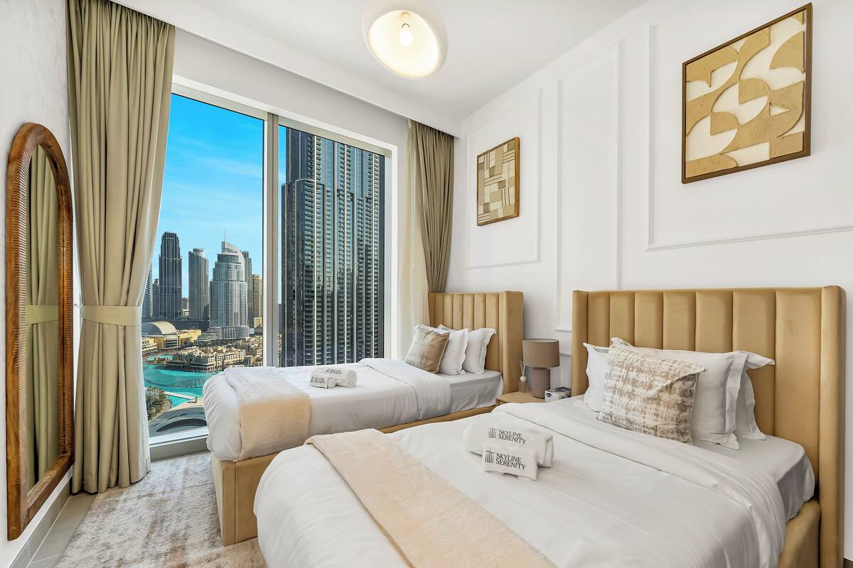 A hotel room with two beds, a view of a cityscape, and a large window with curtains.