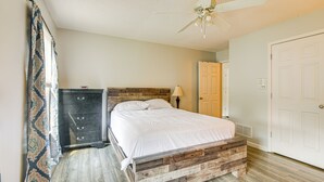 Een slaapkamer met een houten bedframe, een plafondventilator, een dressoir en een deur.