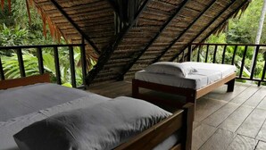 A room with two wooden beds, a thatched roof, and a view of lush greenery. - Maloka Napu-Ecodestinos (Puerto Nariño)