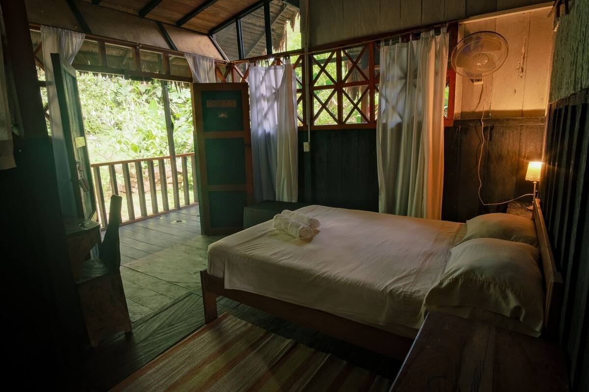 Une pièce en bois avec un lit, un ventilateur et une fenêtre avec des rideaux.
