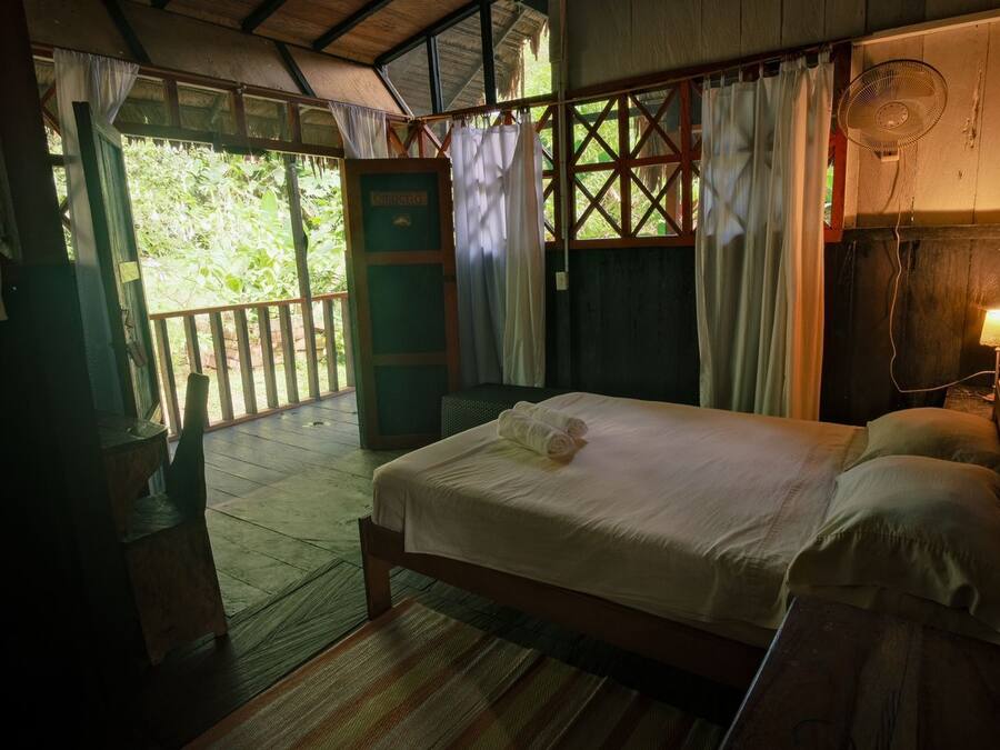 A wooden room with a bed, a fan, and a window with curtains.