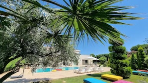 Un área de piscina con sillones de descanso y colchones de colores sobre el césped.