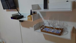 A wall-mounted shelf with a flat-screen TV, a router, and a smartphone. Below, there are wine glasses on a tray. - Kitnet Apartment Copacabana (Copacabana Rio de Janeiro)