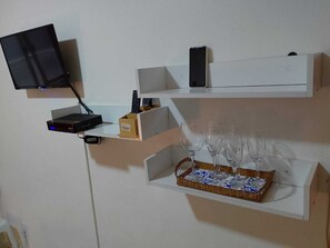 A wall-mounted shelf with a flat-screen TV, a router, and a smartphone. Below, there are wine glasses on a tray.