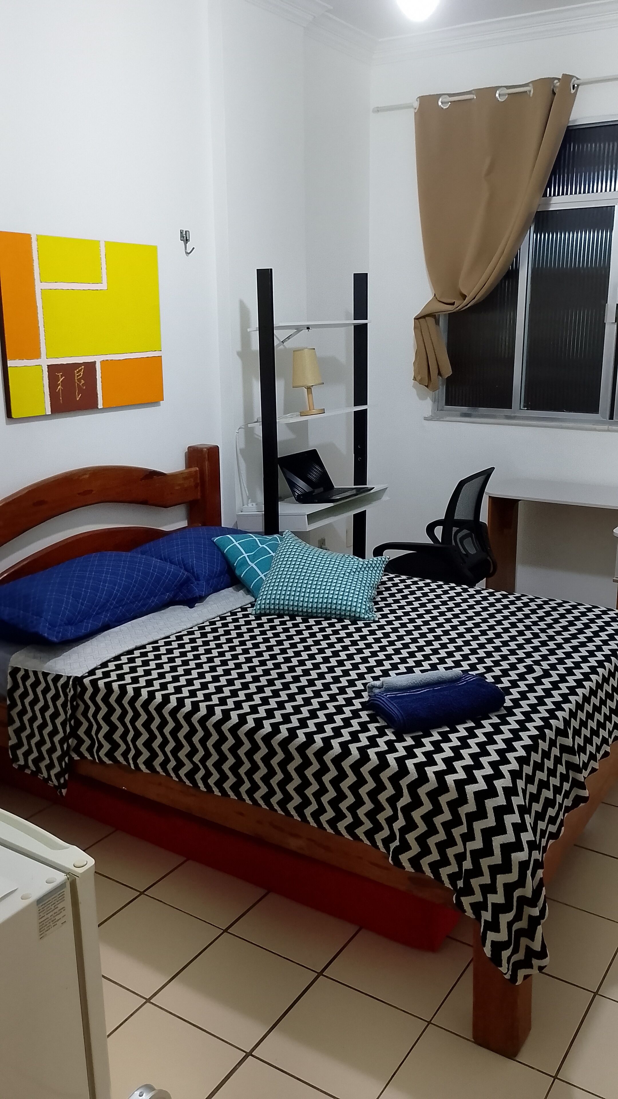 Een slaapkamer met een bed, een bureau, een stoel en een raam met gordijnen.