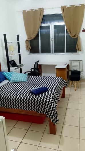Une chambre à coucher avec un lit, un bureau, une chaise, une lampe et une fenêtre avec des rideaux.