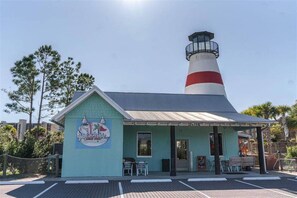 A building with a lighthouse structure, a sign reading "Beachside Mini Golf," and a parking area with a fence.