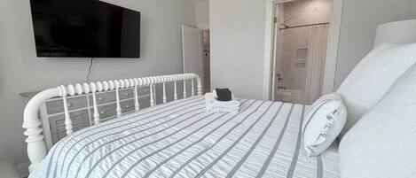 Un dormitorio con una cama, un televisor de pantalla plana montado en la pared y una puerta que da a un baño.
