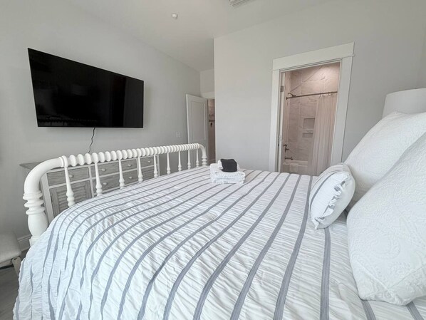 A bedroom with a bed, a flat-screen TV mounted on the wall, and a door leading to a bathroom.
