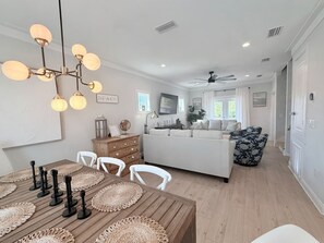 A modern living room with a white sofa, a dining table with placemats, and a ceiling fan.