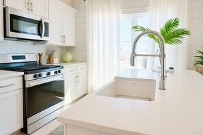 A modern kitchen with white cabinetry, a stainless steel stove, a microwave, and a sink with a modern faucet.