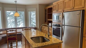 A kitchen with granite countertops, stainless steel appliances, wooden cabinets, and a window with a view of snow-covered trees. - Direct Bike Access, WaterPark, S’mores nights (Bromont)