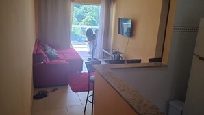 A living area with a red sofa, a flat-screen TV mounted on the wall, and a dining area with a table and chairs.