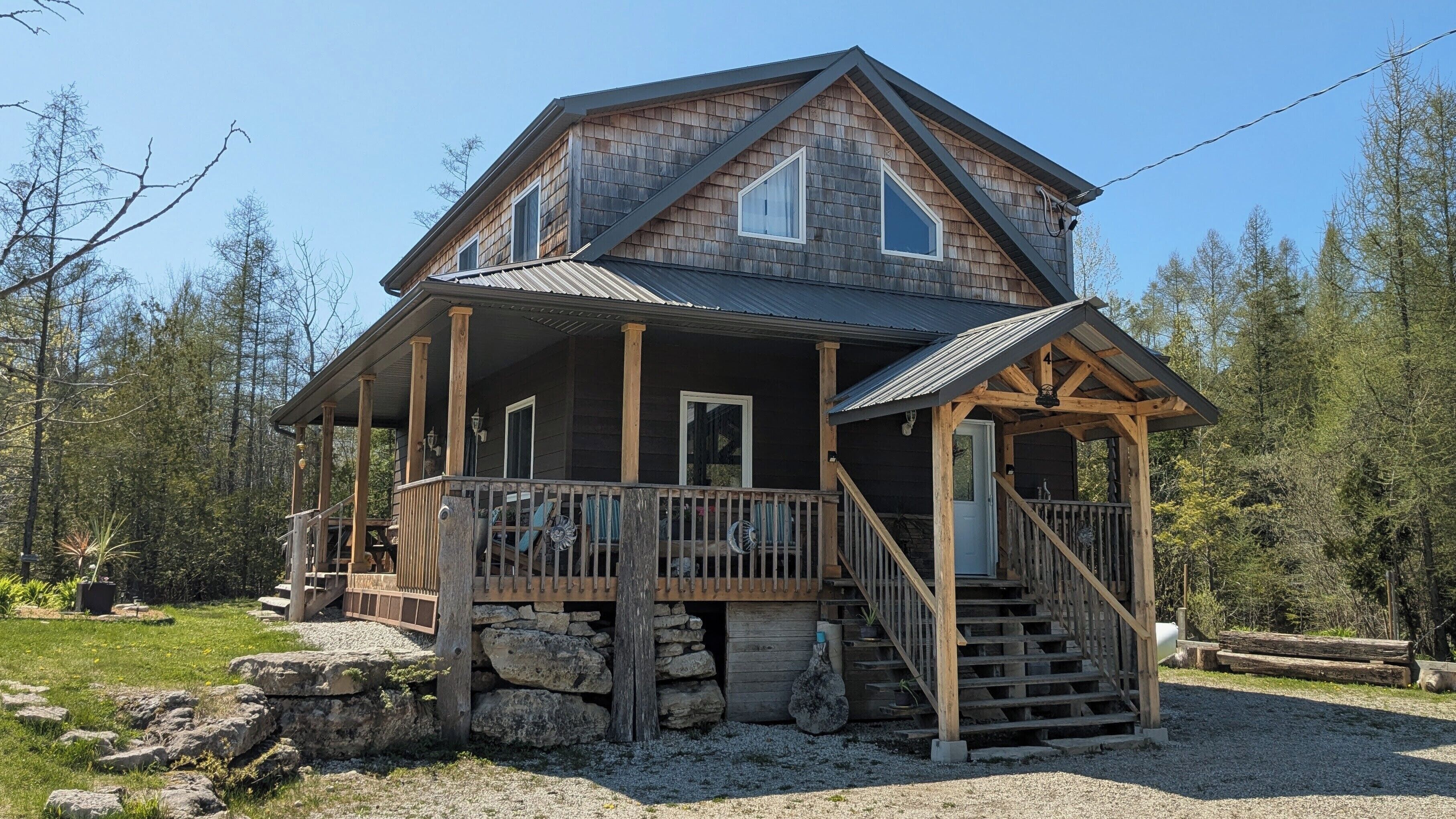 A two-story log cabin with a porch, a staircase, and a stone foundation.