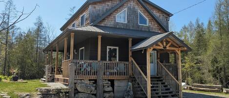 A two-story log cabin with a porch, a staircase, and a stone foundation.