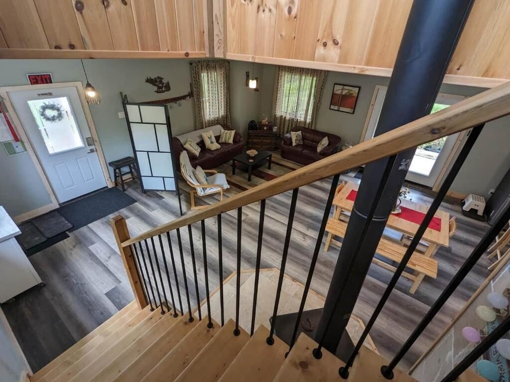 Uma escadaria com corrimão de madeira leva a uma sala de estar com sofá, mesa de centro e mesa de jantar.