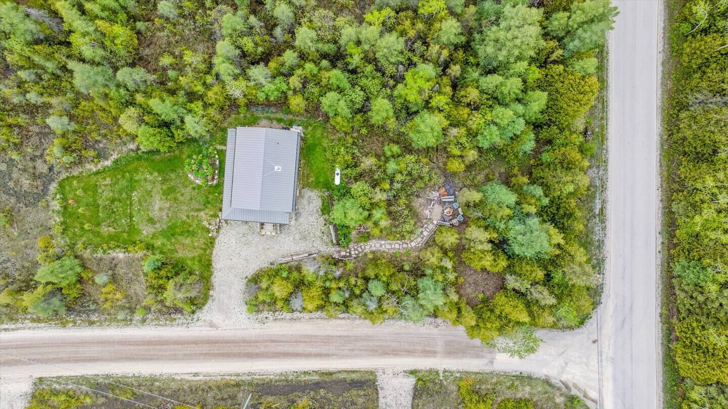 An aerial view of a property with a large building, a paved driveway, and dense surrounding vegetation.