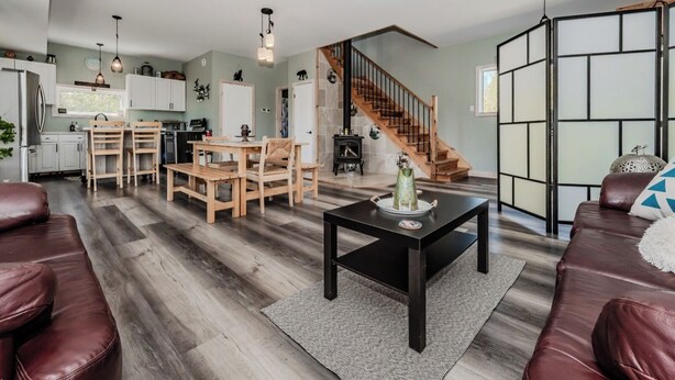 A spacious living area with a wooden dining table, leather sofas, and a staircase leading to an upper level.