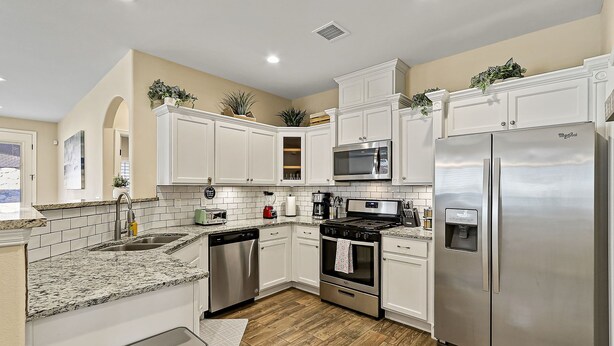 A modern kitchen with white cabinets, stainless steel appliances, and a granite countertop.