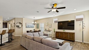 A modern living room with a sectional sofa, a dining area, a kitchen, and a ceiling fan.