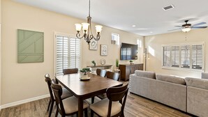 A dining area with a wooden table and chairs, a chandelier, and a sofa in the background.