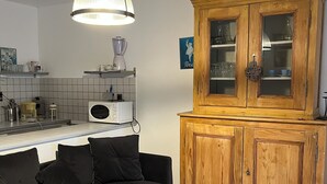 A modern kitchen with a black sofa, wooden cabinet, and a hanging light fixture. - Studio in the countryside near village with all amenities (Sénas)