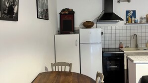 A compact kitchen with white cabinets, a black stove, and a white refrigerator. There is a wooden dining table with chairs and a black oven. - Studio in the countryside near village with all amenities (Sénas)